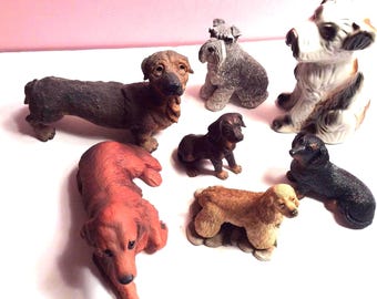 May include: A collection of seven ceramic dog figurines. The figurines are in various poses and breeds, including a dachshund, a schnauzer, a cocker spaniel, and a terrier. The figurines are painted in realistic colors and have detailed features.
