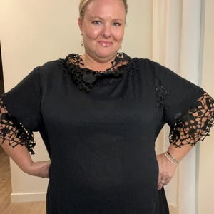 May include: A black dress with a lace collar and lace trim on the sleeves. The dress has a scoop neck and a relaxed fit.