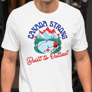 Op de afbeelding: Wit T-shirt met een afbeelding van een Canadees landschap en de tekst "Canada Strong Built to Outlast".