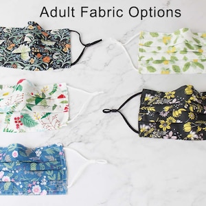 May include: Five different fabric options for face masks. The masks are pleated and have different floral patterns. The fabrics are black with yellow flowers, white with red berries and green leaves, blue with pink flowers and green leaves, green with yellow flowers, and dark green with orange and white flowers.