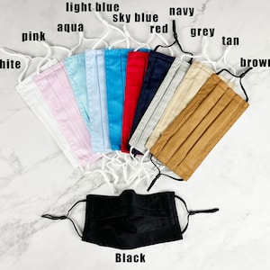 May include: A set of 10 face masks in various colors, including white, pink, aqua, light blue, sky blue, red, navy, grey, tan, and brown. A black face mask is also shown in the center of the image.  The masks are all pleated and have elastic ear loops.