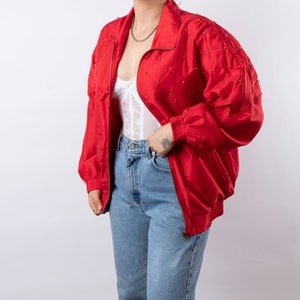 May include: A red satin bomber jacket with gold accents. The jacket has a zipper closure and a stand-up collar.