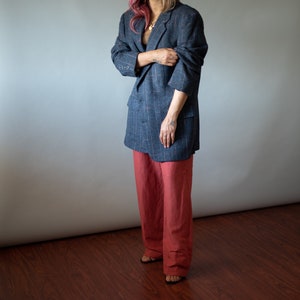 Op de afbeelding: Een vrouw draagt een blauwe geruite blazer met een rood en wit patroon en een rode wijde broek.
