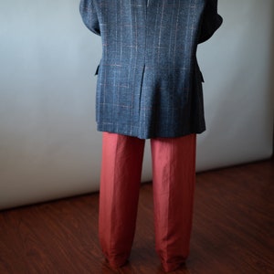 Op de afbeelding: Een grijs geruit blazer met een rood-wit patroon, gedragen over een rode broek.