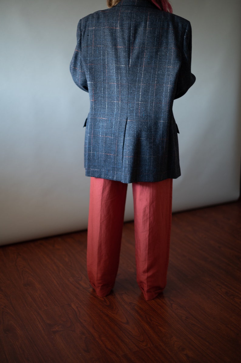 Op de afbeelding: Een grijs geruit blazer met een rood-wit patroon, gedragen over een rode broek.