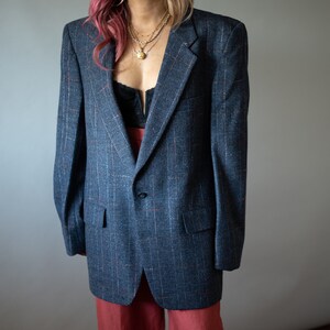 Op de afbeelding: Een blauwe blazer met een subtiel ruitpatroon. De blazer heeft een enkele knoopsluiting en een revers.