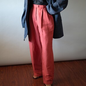 Op de afbeelding: Een vrouw draagt een donkerblauwe blazer over een zwarte kanten top en een hoge taille, wijde terracotta broek.