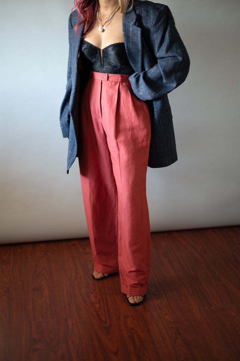 Op de afbeelding: Een vrouw draagt een donkerblauwe blazer over een zwarte kanten top en een hoge taille, wijde terracotta broek.