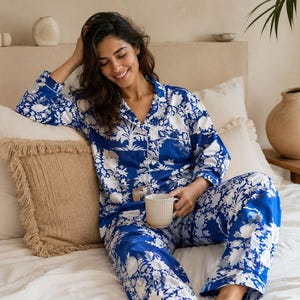 Könnte beinhalten: Ein zweiteiliger Schlafanzug bestehend aus einem langärmeligen, geknöpften Oberteil und einer passenden Hose mit einem leuchtend blauen und weißen Blumenmuster. Das Oberteil hat einen Reverskragen, eine Brusttasche und weiße Paspeln.