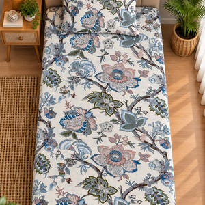 Può includere: Un set composto da lenzuolo e federa abbinata con sfondo color crema e un motivo floreale ripetuto nelle tonalità del blu polvere, rosa tenue e verde salvia. Il design botanico presenta grandi fiori stilizzati e rami con foglie.
