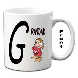 May include: White ceramic mug with a black letter G and the word "RANDAD" printed on the front. A cartoon image of a dwarf with a red and white outfit is also on the front of the mug. The word "Front" is printed on the handle of the mug.