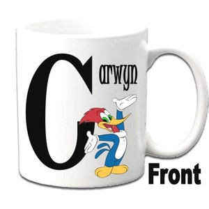 K&ouml;nnte beinhalten: Eine wei&szlig;e Keramiktasse mit einem schwarzen Buchstaben C und einem Cartoon-Bild von Woody Woodpecker. Die Tasse tr&auml;gt den Namen "Carwyn".