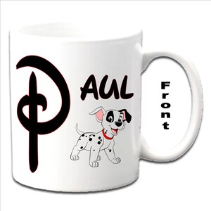 Pode incluir: Caneca de cerâmica branca com um 'D' preto estilo Disney no lado esquerdo, o nome 'PAUL' em texto preto e um filhote de dálmata de desenho animado no lado direito. A palavra 'Front' está escrita verticalmente na alça.