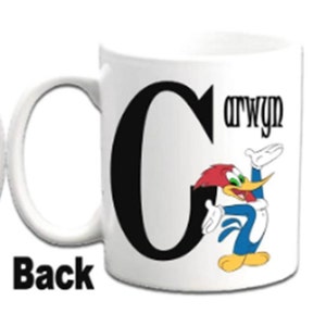K&ouml;nnte beinhalten: Wei&szlig;e Keramiktasse mit einem schwarzen Buchstaben C und einem Cartoon-Bild von Woody Woodpecker. Die Tasse tr&auml;gt den Namen "Carwyn" in Schwarz auf der Seite.