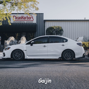 May include: A white Subaru WRX with black wheels parked in front of a building with the sign "Clean Harbors Environmental Services".