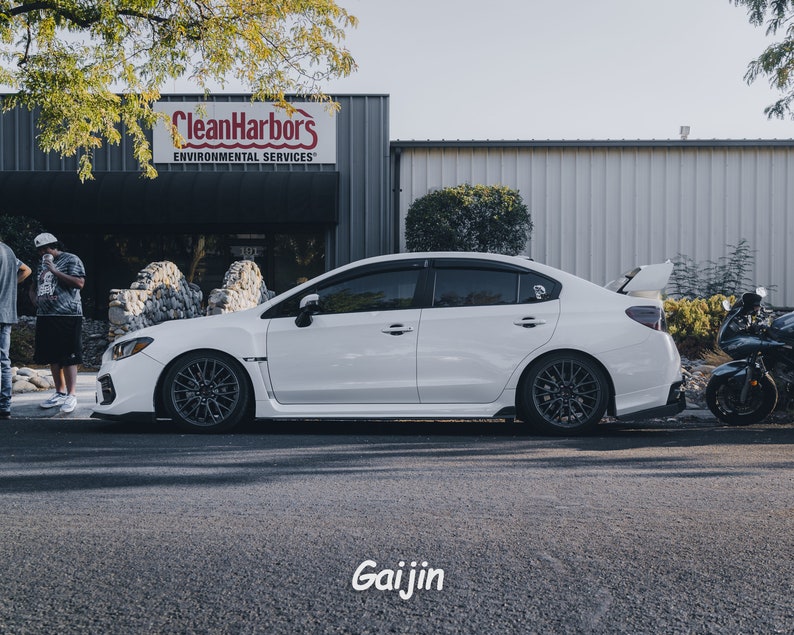 May include: A white Subaru WRX with black wheels parked in front of a building with the sign "Clean Harbors Environmental Services".