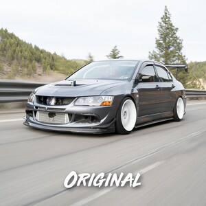 K&ouml;nnte beinhalten: Ein grauer Mitsubishi Lancer Evolution, ein beliebtes Sportwagenmodell, f&auml;hrt auf einer kurvigen Stra&szlig;e mit B&auml;umen und H&uuml;geln im Hintergrund. Das Auto hat einen gro&szlig;en Heckspoiler und wei&szlig;e R&auml;der.