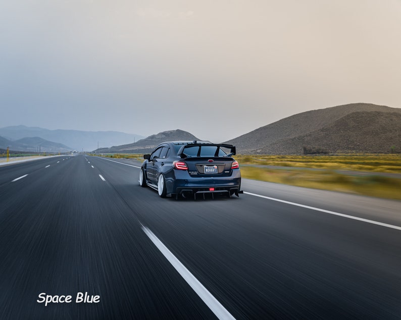 May include: A dark blue Subaru WRX STI driving on a highway with mountains in the background. The car has a rear spoiler and a license plate that reads "WRX STI".