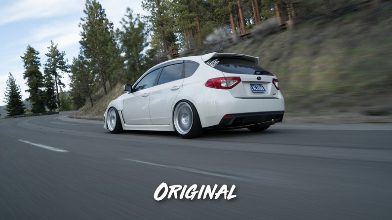 K&ouml;nnte beinhalten: Ein wei&szlig;er Subaru Impreza WRX STI Kombi f&auml;hrt auf einer kurvigen Stra&szlig;e durch einen Wald. Das Auto hat einen schwarzen Heckspoiler und schwarze Felgen.