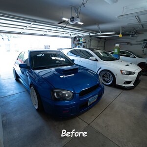 May include: A blue Subaru Impreza WRX STI and a white Mitsubishi Lancer Evolution parked in a garage. The Subaru has a white racing stripe on the hood and the Lancer has blacked-out windows.
