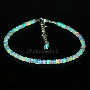 May include: A delicate opal beaded bracelet with a silver clasp. The beads are iridescent and reflect a rainbow of colors.