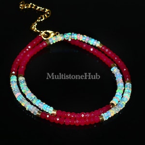 May include: A double-strand necklace with red and white beads. The necklace is made of red gemstone beads and white opal beads. The necklace has a gold clasp.