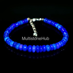 May include: A blue opal gemstone bracelet with a silver clasp. The bracelet is made of round beads and has a subtle iridescent sheen.
