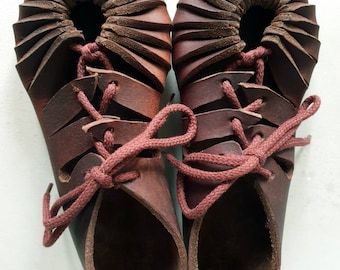 May include: A pair of brown leather sandals with laces. The sandals have a unique design with a pleated top and a cut-out pattern.