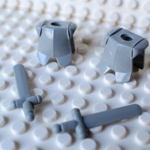 May include: Two gray plastic toy armor pieces and two gray plastic toy swords on a white background.