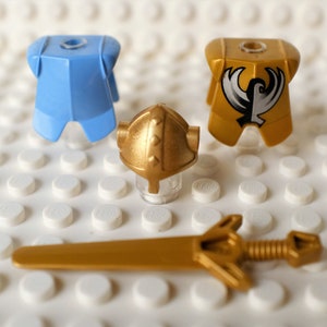 May include: A set of three gold-colored LEGO minifigure accessories: a helmet, a chest piece with a white bird design, and a sword. The chest piece is also available in light blue.