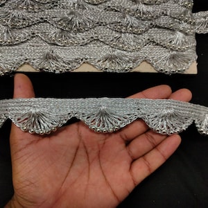 Pode incluir: Bordado de contas prateadas com borda festonada e detalhe de franja. O bordado é feito de um tecido delicado de crochê e é perfeito para adicionar um toque de elegância a qualquer projeto.