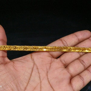 May include: Gold trim with a zig-zag pattern. The trim is shown on a hand.
