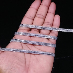 May include: Silver trim with a zig-zag pattern. The trim is shown in a hand, folded over on itself.
