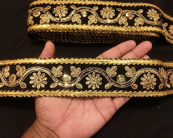 Op de afbeelding: Zwarte fluwelen bies met gouden borduurwerk en pailletten. De bies heeft een herhalend patroon van bloemen en bladeren.