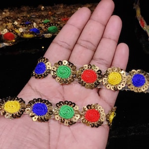 Pode incluir: Renda com acabamento dourado e círculos bordados coloridos. A renda apresenta um padrão repetitivo de círculos azuis, verdes, amarelos e vermelhos.