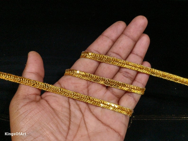May include: Gold-coloured trim with a zig-zag pattern. The trim is shown wrapped around a hand.