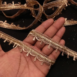 May include: Gold trim with a fringe detail. The trim has a sparkly finish and is perfect for adding a touch of elegance to any project.