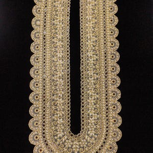 May include: An ornate gold-coloured embroidered neckline with a scalloped edge. The design features floral patterns and small, pearl-like beads. The neckline is set against a black background, highlighting the detailed craftsmanship.