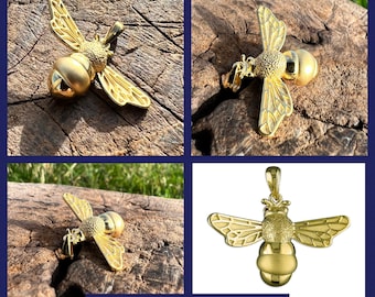 May include: A gold bee pendant charm with detailed wings and a textured body. The charm is shown on a wooden surface.