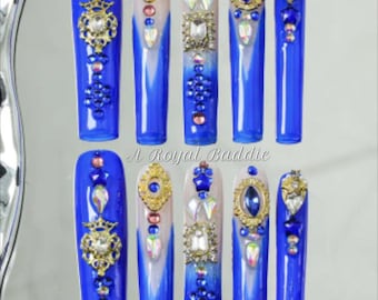 May include: Ten blue and white ombre long false nails with various rhinestones and gold accents.  The nails are decorated with blue, gold, and clear rhinestones, as well as gold accents.  The text "A Royal Baddie" is visible at the bottom of the image.