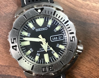 May include: A Seiko automatic diver's watch with a black dial and luminous hands and markers. The watch has a stainless steel bezel with minute markers and a black rubber strap. The date is displayed as SAB 21.