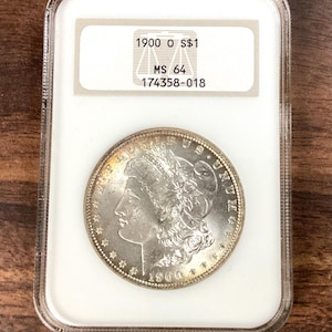 May include: A silver coin from 1900, encased in a clear plastic holder. The coin shows a woman's profile and the text "1900 O S$1". The holder has a label with "MS 64" and other details.