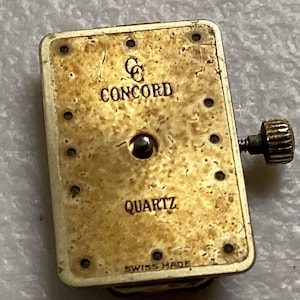 May include: A rectangular watch movement with the brand name "CONCORD" and the word "QUARTZ" printed on the face. The movement is gold-toned with a small crown on the side and the words "SWISS MADE" at the bottom.