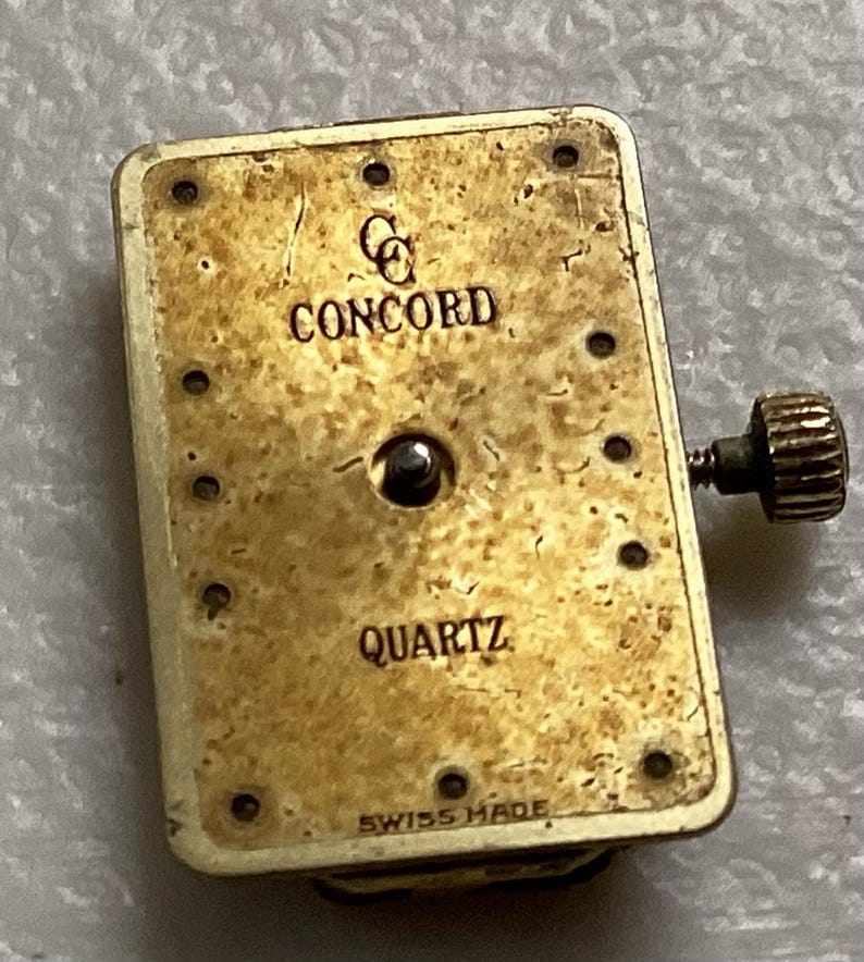 May include: A rectangular watch movement with the brand name "CONCORD" and the word "QUARTZ" printed on the face. The movement is gold-toned with a small crown on the side and the words "SWISS MADE" at the bottom.