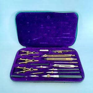Op de afbeelding: Een set messing tekeninstrumenten gerangschikt in een rechthoekige etui met een felpaarse fluwelen binnenkant. De collectie bevat diverse passers, verdelers en precisiegereedschappen met metalen afwerkingen, vastgezet in voorgevormde vakken.