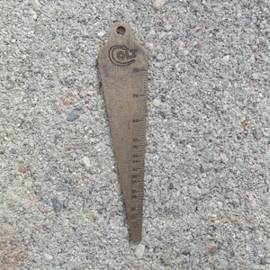 May include: A brass gauge with a Colt logo and a ruler marked in inches. The gauge is a tool for measuring the diameter of objects.