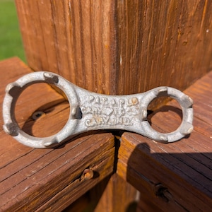May include: A silver-colored metal tool with two circular openings, each featuring four protruding prongs. The central bridge of the tool is embossed with the text PAT APD FOR, GARY IND, and a small heart symbol between the lines of text.