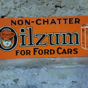 May include: Orange Oilzum sign for Ford cars. The sign features the text "NON-CHATTER Oilzum FOR FORD CARS" in black lettering. A graphic of a man wearing glasses is in a circle. A small oil can graphic is on the right.