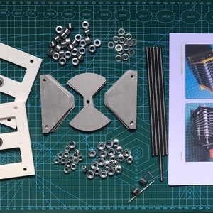 Könnte beinhalten: Ein Satz Teile zum Zusammenbauen eines Schmetterlingskondensators. Die Teile umfassen Metallplatten, Stangen, Muttern und einen kleinen Schraubenschlüssel. Das Bild enthält auch Anweisungen zum Zusammenbauen des Kondensators.