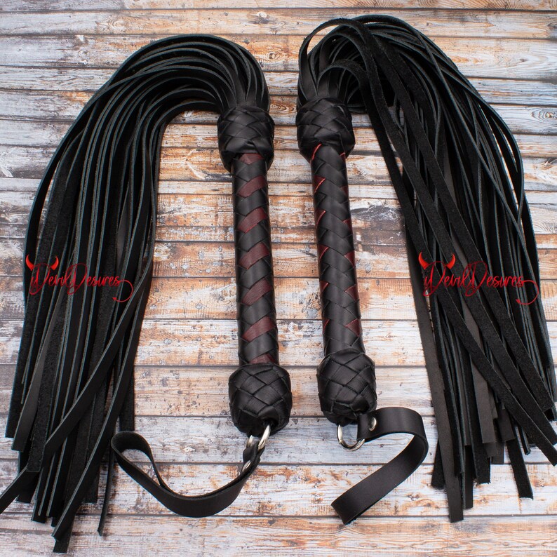 May include: Two black leather whips with braided handles. The handles are black and burgundy. The whips have a silver ring at the end of the handle.
